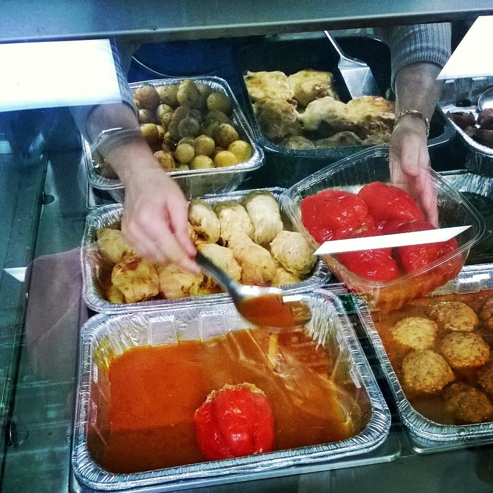 Deli worker plating stuffed peppers and prepared hot dishes behind the counter